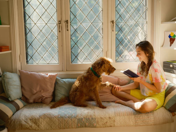 WOman reading book while the dog sits besides her on the sofa