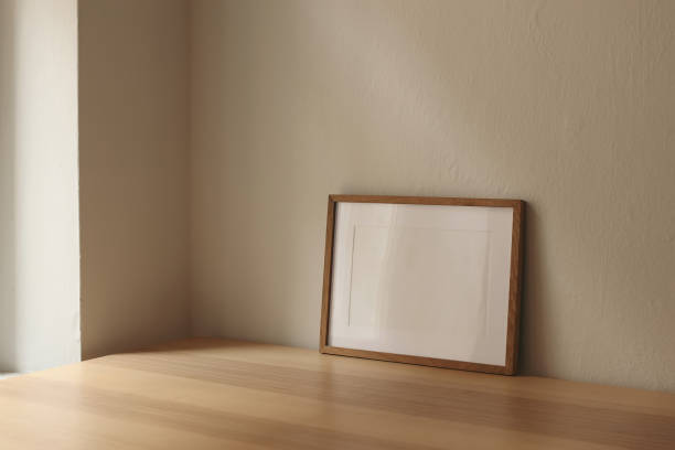 istock Horizontal wooden thin picture frame, empty poster mockup on wooden table near window. Beige wall background. Modern moody interior decor. Side view, copy space, no people. Minimal composition. 2183288482