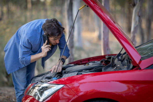 istock A young man on vacation tries to fix his car when it breaks down. 2183295538