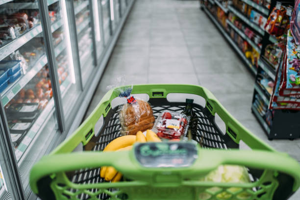 Shot of a shopping cart with groceries in the middle of the aisle in the supermarket. No people on the photo.