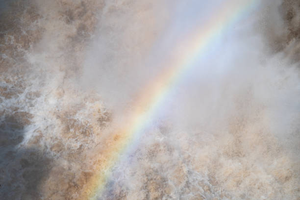 A stunning waterfall gracefully cascades down, with a vibrant rainbow brilliantly arching through the mist that surrounds it