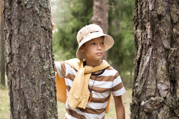A little boy on a walk in the forest or park, peeking out from behind a tree.