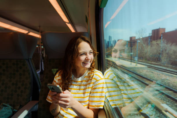 Woman using smartphone and looking through the window traveling by train in Canada