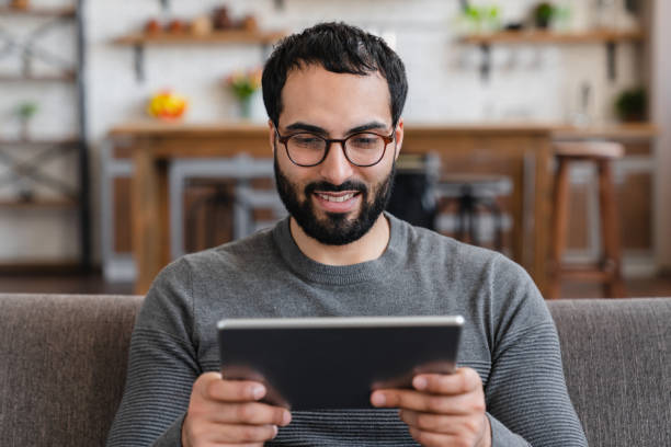 istock Millennial smiling guy rest on sofa at home with tablet enjoy weekend use internet services 2183306899