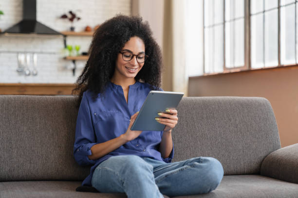 istock Happy Black girl relaxing sofa using tablet computer reading e-book watching movie chatting online 2183307012