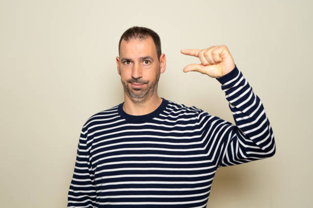 istock Bearded hispanic man in his 40s wearing a striped sweater with an annoyed expression making a size sign with his hand with his fingers while looking at the camera. Measurement concept 2183308241