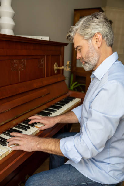 istock Gray-haired mature man playing the piano and looking involved 2183310118