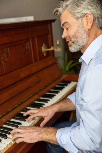 istock Gray-haired mature man playing the piano and looking involved 2183310119