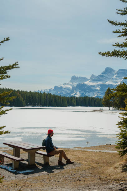 istock Man looks at lake covered with ice in mountains sitting on the bench 2183325921