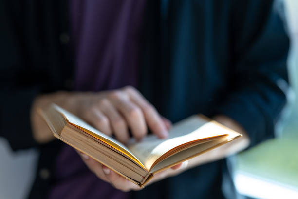 This is a close up photograph of the hands of a young African American woman in her 20s reading a book outdoors in Central Park on an October day in New York City, USA