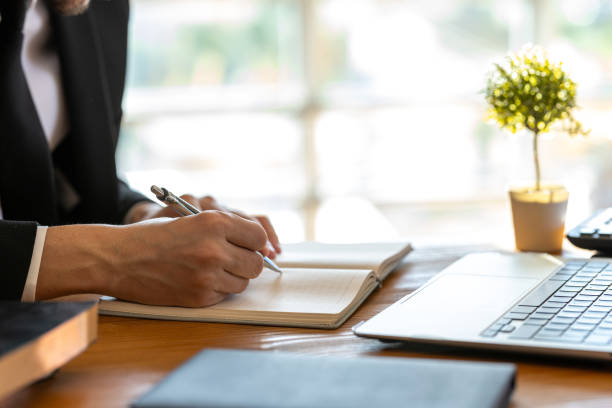 istock Unknown businessman taking notes in his notebook while working at his desk in his home office 2183327350