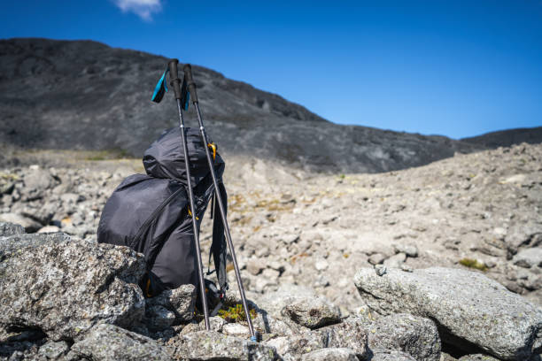 A backpack and trekking poles rest on rocky terrain under a clear blue sky, symbolizing adventure and exploration in a mountainous landscape.