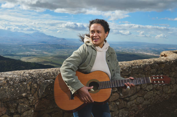 istock Smiling woman playing guitar outdoors with scenic mountain backdrop 2183336052
