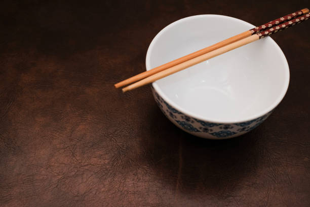 White bowl with blue pattern outside and wooden chopsticks on brown background, traditional wooden sticks for asian food.