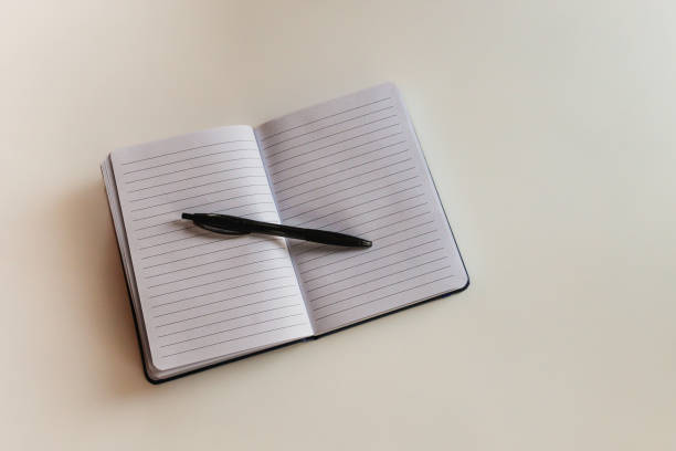 A lined open notepad book with a black pen placed on white isolated table. Idea of planning, back to school, business concept, brainstorming, future, mapping, diary concept.
