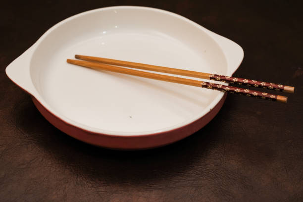 Empty white ceramic plate with  handle on the side and wooden chopsticks on the brown background, traditional wooden sticks for asian food.