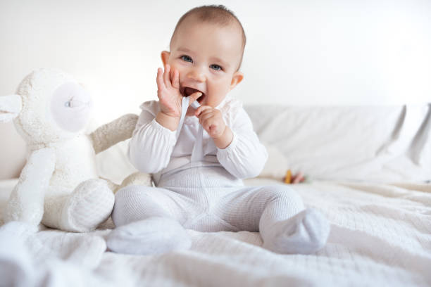 istock Adorable Baby Playing with Hands and Stuffed Animal on Bed 2183345258