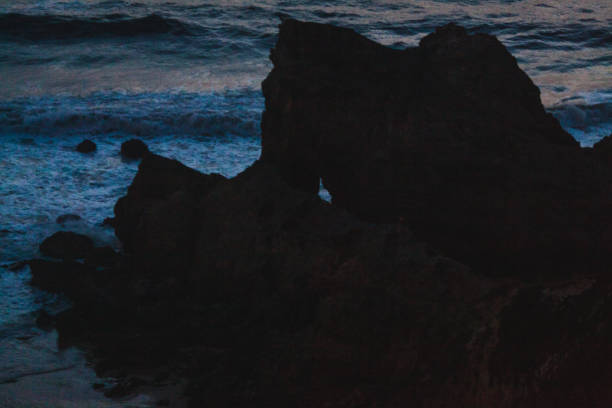low-light photograph captures a rugged coastal rock formation against a dimly lit ocean backdrop