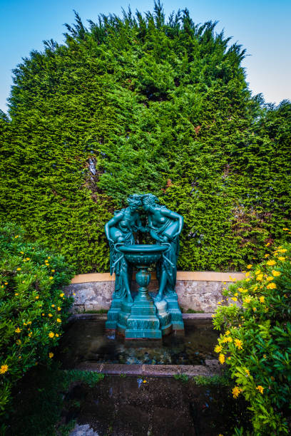 istock green statue of two classical female figures in an intimate pose, each leaning towards a basin they hold together. The figures are draped in flowing garments that enhance the sense of movement and grace in the sculpture 2183347293