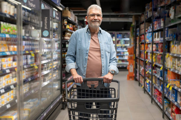 istock Smiling senior man pushing a cart down a brightly lit grocery store aisle 2183349943