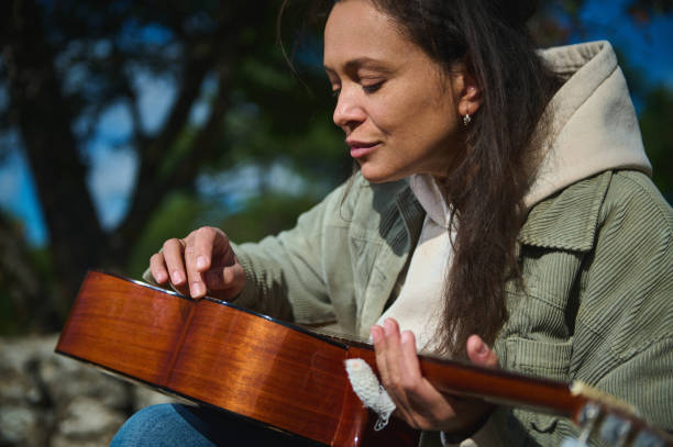 Woman playing guitar outdoors with nature in the background