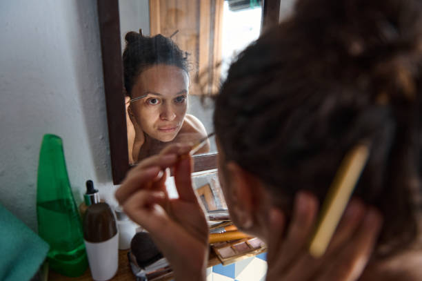 Woman applying makeup with concentration in front of a mirror