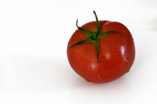 A vibrant red tomato rests alone, highlighting its fresh texture and glossy surface against a plain background.