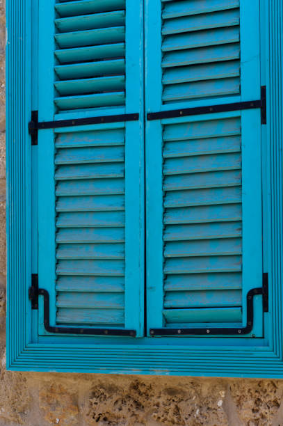 Vibrant blue shutters against rustic stone wall in a sunlit Mediterranean village