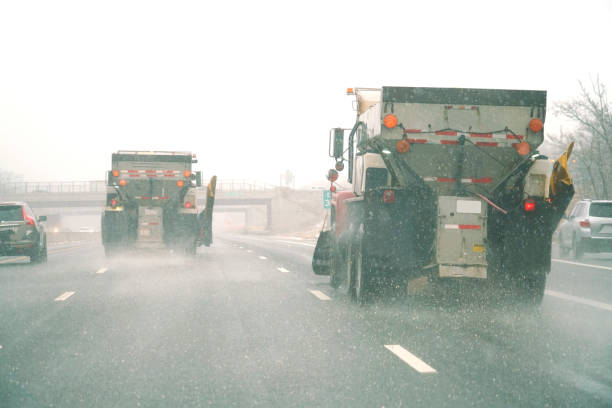 Car driver point of view looking through windshield at approaching semi tractor trailer truck speeding past and kicking up road spray during a heavy winter blizzard snow storm on a stretch of rural western New York State highway.