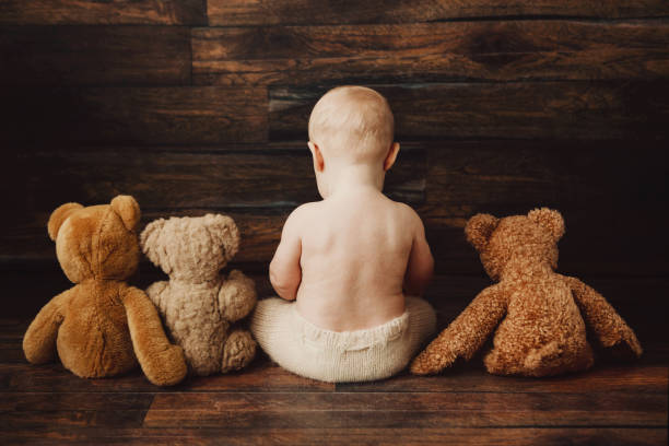 smiling baby girl 6 months old lies on a white isolated background in a bright bodysuit with a soft Teddy bear, space for text