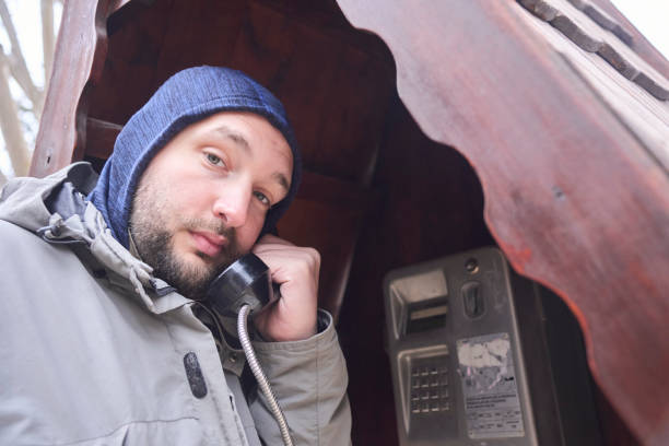 Young man looking at the camera testing the line of an old obsolete payphone in a phone booth. Nostalgia for old technologies.