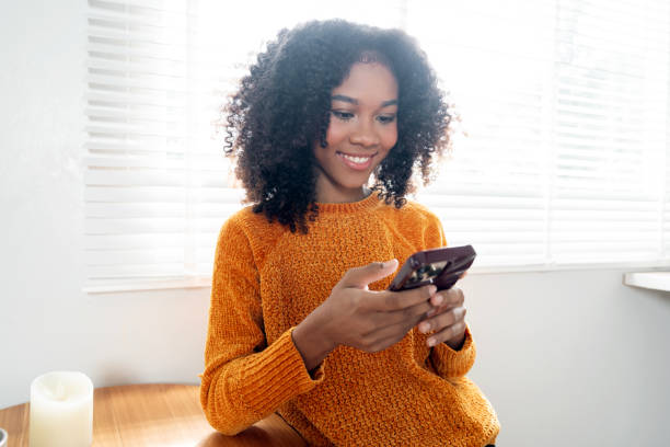 istock Happy young black woman using mobile phone relaxing on sofa at home. 2183393681