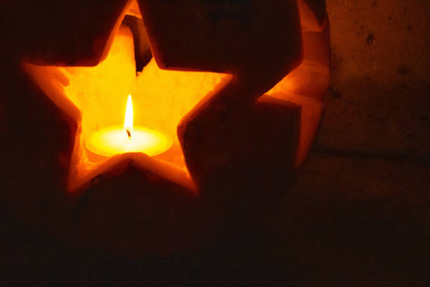 A close-up of a pumpkin carved with a star shape, glowing from the light of a candle placed inside. The soft, warm light creates a cozy and festive atmosphere.