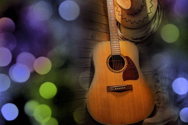 Acoustic guitar, lasso, cowboy hat and boots on a barn wood background. American Country music concept. Beautiful bokeh lights, space for copy.
