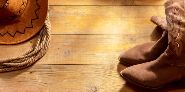 istock Cowboy hat and boots with a rope on a barn wood background 2183418542