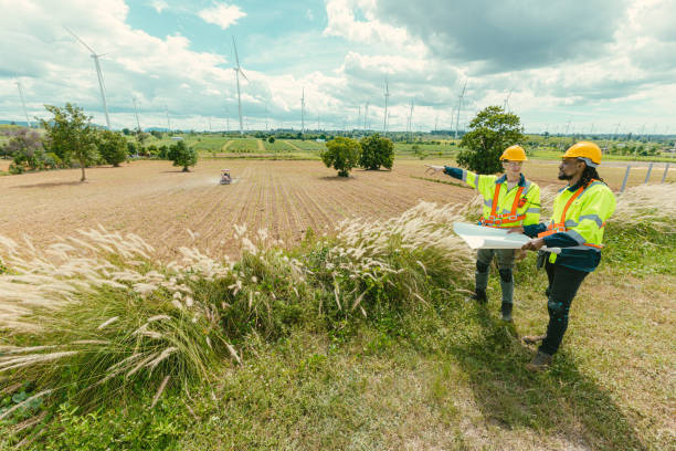 istock Engineer team mix black and white male workers with floor plan at Wind Turbines field working survey at wind electricity generator farm field outdoor. 2183419665