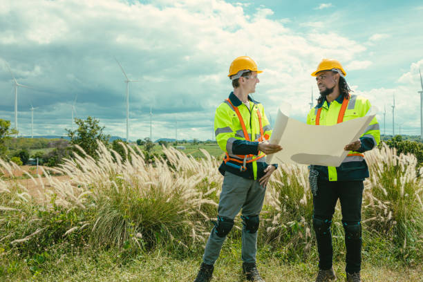 istock Engineer team mix black and white male workers with floor plan at Wind Turbines field working survey at wind electricity generator farm field outdoor. 2183419673