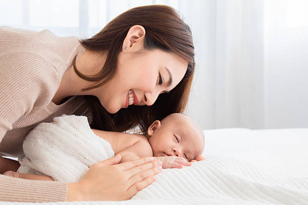 istock Selective focus of newborn baby deep sleeping on white bed. Asian beautiful mother hugging, cuddling and gently holding adorable infant hand with soft and care. Child healthcare sleep in mom's hand 2183420563
