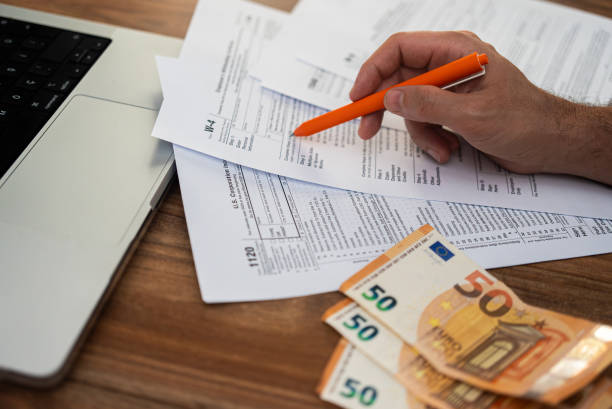 istock Office worker hand points with pen at tax forms near euro banknotes examining steps of filling blank 2183425668