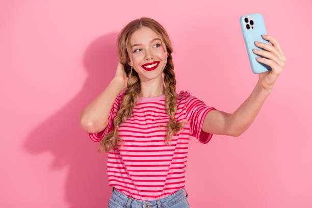 istock Charming young woman taking a selfie with smartphone against pink background, showcasing a fun and stylish look with braided hair. 2183429700