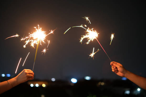 Shot of unrecognizable couple hands Playing Sparklers on New Year Eve. Concept: celebration, couple bonding,celebrating anniversary,birthday, festive lights, holiday tradition, joy, nighttime glow, fireworks, togetherness, magical moments, sparkler light