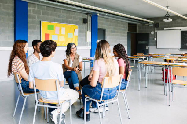 Young group of teenage students discussing in classroom with teacher stock photo