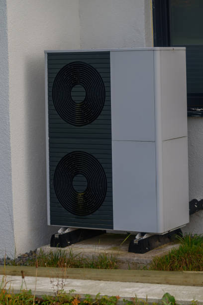 istock Outdoor heat pump with two ventilation grilles on a concrete base, surrounded by vegetation, with green spots likely from algae or moss due to moisture and weather exposure. 2183441868