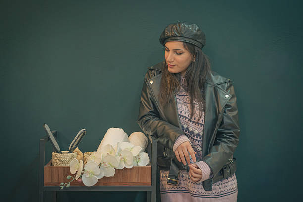 A stylish woman in a leather jacket and cozy sweater standing beside a spa setup with beauty tools and orchids, creating a serene and elegant self-care scene.