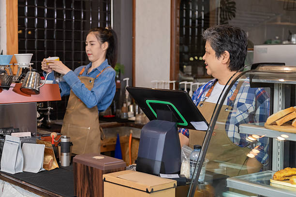 istock Young attractive barista working together with senior elderly retirement woman while using POS matching cash register technology to receive customer orders, happy 60s aging society people working 2183444437