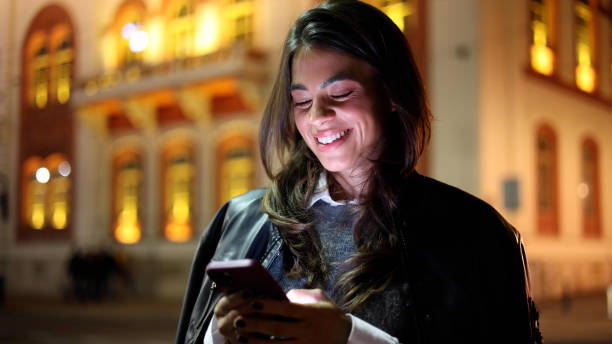 istock Woman walking through the city lights, using smartphone with a smile 2183447253