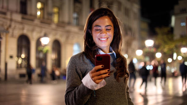 istock Woman walking through the city lights, using smartphone with a smile 2183447325