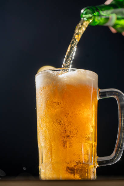 istock A bright and refreshing beer is being poured into a cold glass mug. The golden liquid, illuminated by a dark background, perfectly captures the celebratory essence of Beer Fest. 2183449411