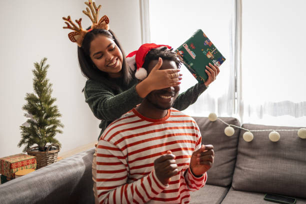 istock Young woman covers her boyfriend's eyes while giving him a Christmas present 2183456129
