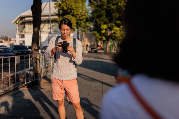 Thai man takes a photograph with a camera of his girlfriend while standing on the historic streets of Bangkok.
